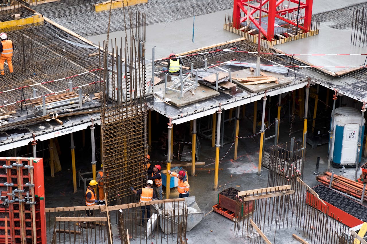 portfolio-05 Workers in high visibility gear at a busy construction site with scaffolding and steel frames.